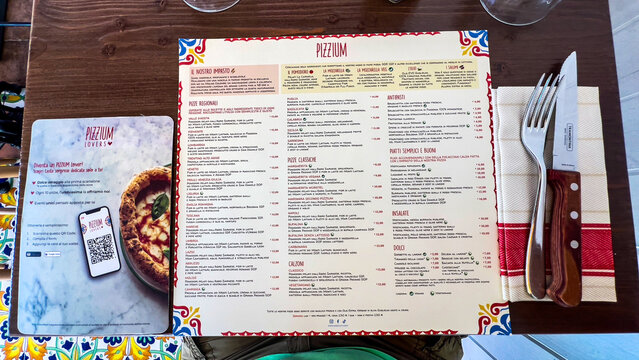 PIZZIUM restaurant table setting featuring an authentic Italian menu card and cutlery resting on a rustic wooden surface set in a European eatery