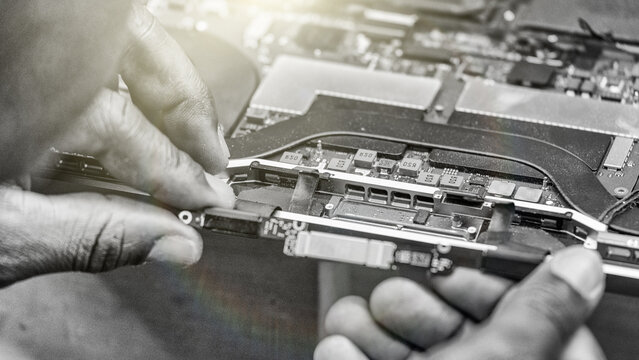Back view of technician repairing laptop in electronics workshop with tools