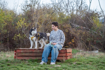 Husky stands on bench above teenage boy looking down at him, bonding built without single command, comfort of living with dog. Wide shot. Concept of bonding of teenager with his dog © iwavephoto