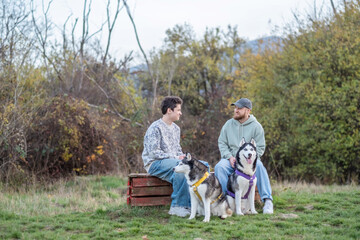 Father and teenage son look at each other resting with their dogs, generation talking instead of arguing, moment building real trust. Wide shot. Concept of generation talk during dog walk © iwavephoto