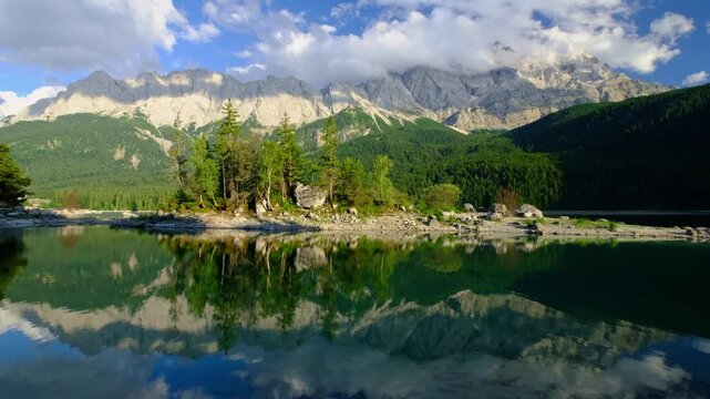 Static shot of a small island in Eibsee lake reflecting the Zugspitze mountains and blue sky in the Bavarian Alps, Germany.