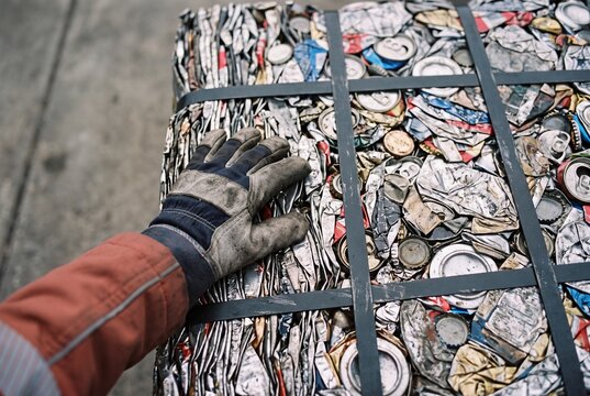 Worker in protective gloves touching a compacted bale of recycled crushed aluminum cans at a waste management facility