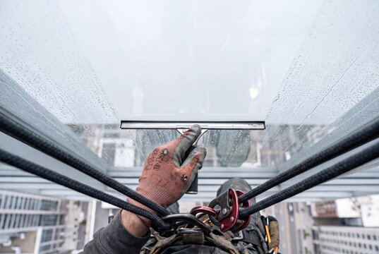 Professional industrial rope access window cleaner washing high-rise modern building glass facade with a squeegee tool