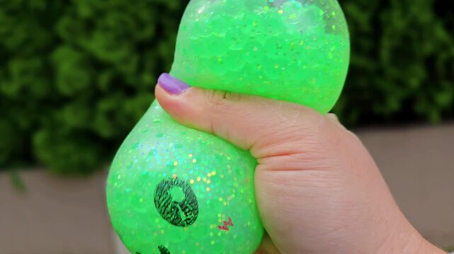 green glitter kawaii squishy toy with cute smiley face and rosy cheeks held in hand, sparkly round ball squished outdoors