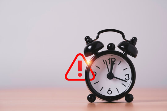 Alarm clock with warning symbol represents deadline urgency, time management, risk and time pressure with copy space for business planning, productivity schedule and reminder concepts.