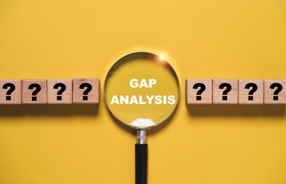 Gap analysis under magnifying glass with question mark blocks represents identifying performance gaps, problems and opportunities for business strategy, assessment, improvement and decision making.