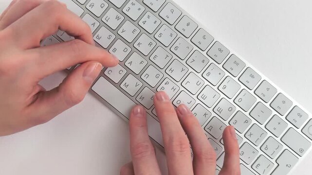 Hurried typing on a wireless desktop keyboard by a stressed worker facing deadline. Female hands press buttons rapidly to finish a journalistic report or copywriting text. Overhead