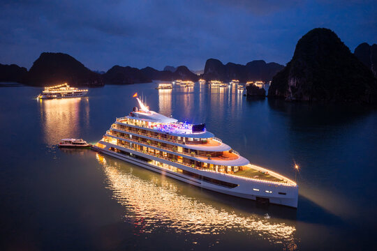 Aerial view of illuminated cruise ships anchored in Ha Long Bay, Vietnam, at dusk with dramatic sunset clouds and limestone karsts