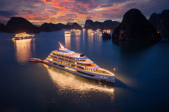 Aerial view of illuminated cruise ships anchored in Ha Long Bay, Vietnam, at dusk with dramatic sunset clouds and limestone karsts