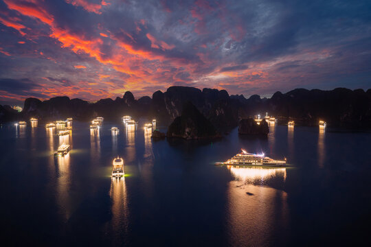 Aerial view of illuminated cruise ships anchored in Ha Long Bay, Vietnam, at dusk with dramatic sunset clouds and limestone karsts