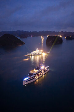 Aerial view of illuminated cruise ships anchored in Ha Long Bay, Vietnam, at dusk with dramatic sunset clouds and limestone karsts