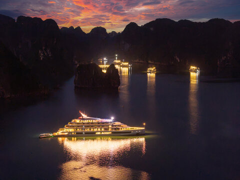 Aerial view of illuminated cruise ships anchored in Ha Long Bay, Vietnam, at dusk with dramatic sunset clouds and limestone karsts
