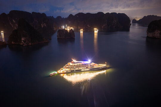 Aerial view of illuminated cruise ships anchored in Ha Long Bay, Vietnam, at dusk with dramatic sunset clouds and limestone karsts