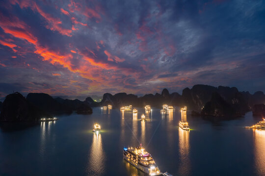 Aerial view of illuminated cruise ships anchored in Ha Long Bay, Vietnam, at dusk with dramatic sunset clouds and limestone karsts