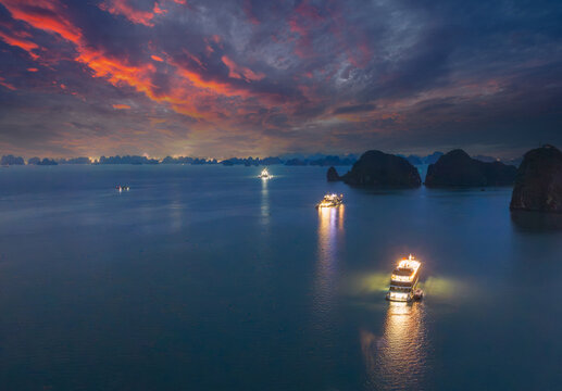 Aerial view of illuminated cruise ships anchored in Ha Long Bay, Vietnam, at dusk with dramatic sunset clouds and limestone karsts
