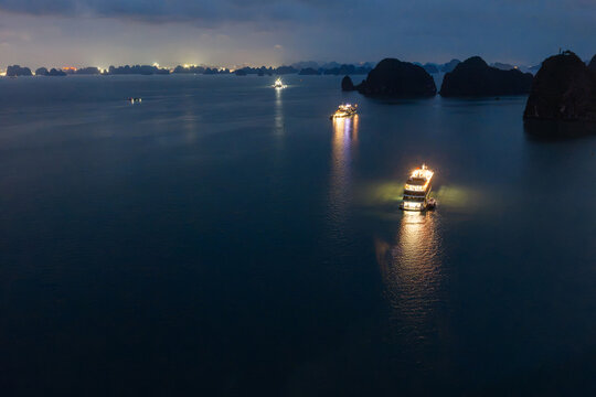 Aerial view of illuminated cruise ships anchored in Ha Long Bay, Vietnam, at dusk with dramatic sunset clouds and limestone karsts