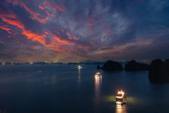 Aerial view of illuminated cruise ships anchored in Ha Long Bay, Vietnam, at dusk with dramatic sunset clouds and limestone karsts