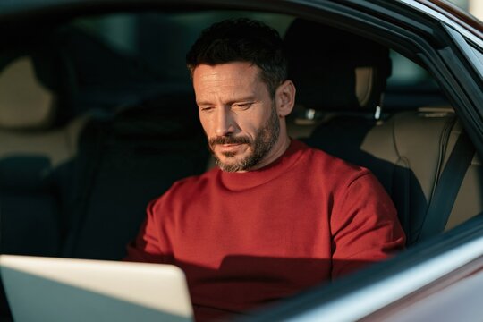 Man working on laptop inside parked car for mobile office background and remote work productivity