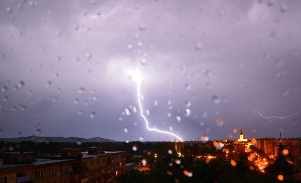 Massive lightning strike illuminating the night sky above city spires through rain