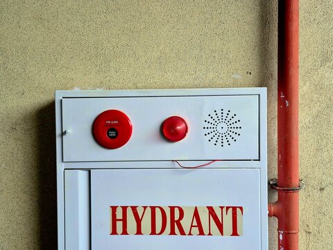 White fire hydrant cabinet with emergency alarm bell and light on a beige wall