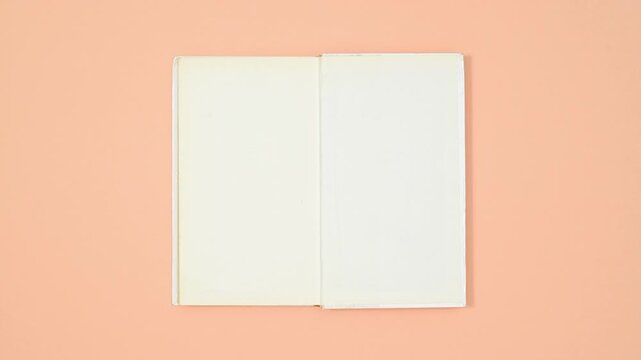 An open book with empty white pages placed flat on an orange background, top view