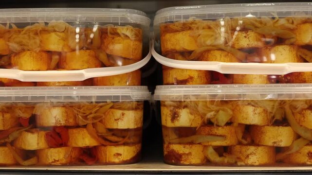 Marinated cheese with cabbage peppers and spices fills clear plastic containers on a supermarket deli shelf offering a savory ready to eat food for quick convenient meals