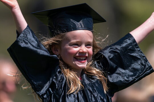 Joyful Young Girl in Cap and Gown Holding Diploma on Vibrant Graduation Day with Beaming Smile and Colorful Balloons in Background