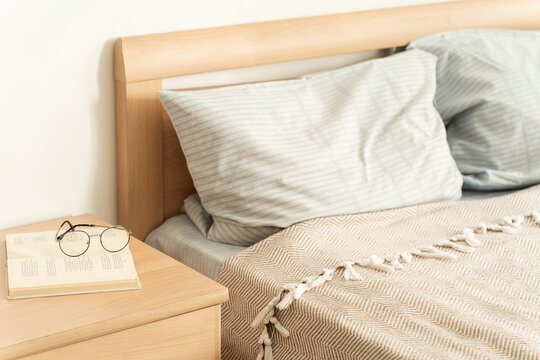Cozy bedroom interior showcasing a wooden bed, patterned blanket, pillows, nightstand with an open book and glasses, symbolizing relaxation. Slow living and mindful lifestyle