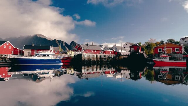 Aerial drone shot moving backward and ascending over scenic fishing village with red wooden houses and boats in Norway during daylight