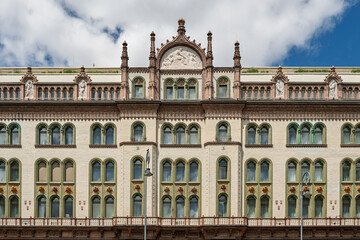 Sculpted figures and arched windows on the Brudern House facade beneath a cloudy sky in Budapest, Hungary © Guillaume Angleraud