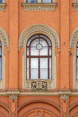 Obraz premium Ornate arched window with a carved coat of arms on a terracotta-colored historicist building facade in Budapest, Hungary