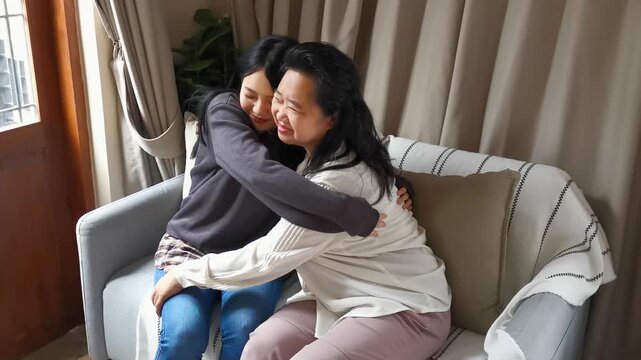 asian senior mother hugging her 20s daughter on sofa in living room, warm family love and bonding