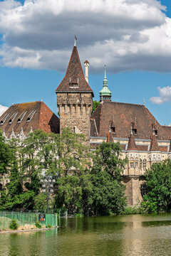 Stone corbelled tower of Vajdahunyad Castle rising above trees beside the lake in City Park Budapest