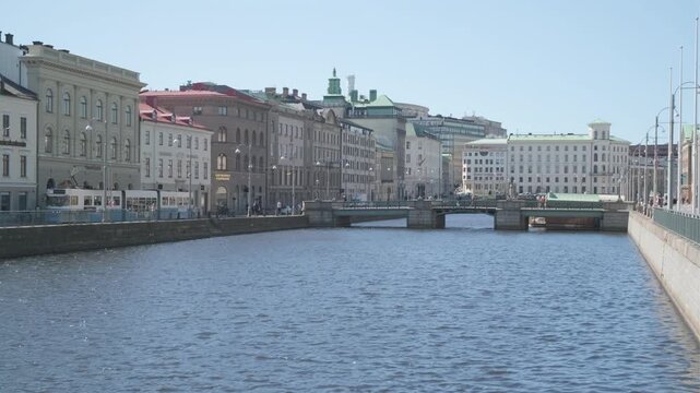 Gothenburg, Sweden - May 2 2023: A calm canal lined with historic buildings and a stone bridge in central Gothenburg, with a tram visible along the waterfront under a clear blue sky
