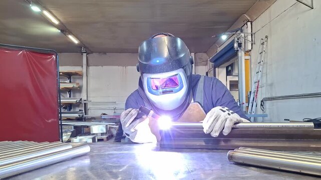 TIG welding process on metal pipe performed by professional worker with mask