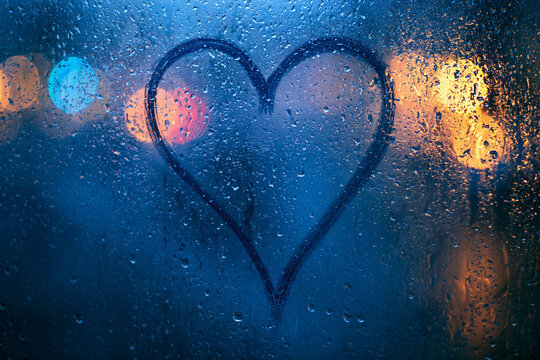 Modern love background with heart on fogged rainy window and colorful urban bokeh