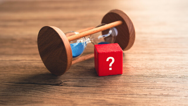 Red question mark block with hourglass lying down on wooden background time management uncertainty countdown deadline concept