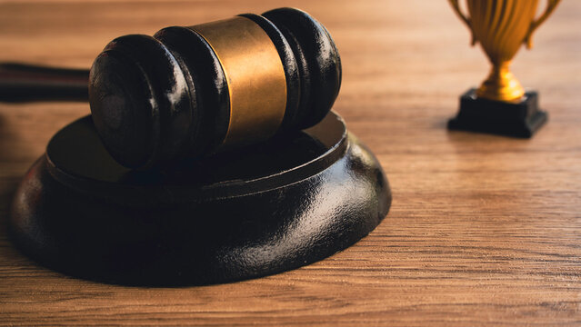 Wooden judge gavel and golden trophy award on desk for legal achievement concept