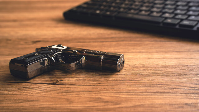 Handgun pistol resting near computer keyboard on wooden table for cyber crime concept