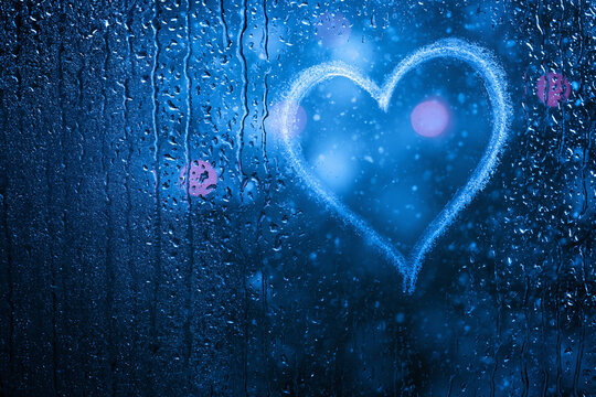 Moody winter romance background with heart on rainy window and blurred Christmas lights