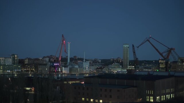 Gothenburg, Sweden - May 2 2023: Two industrial harbor cranes rise above the illuminated Gothenburg skyline at dusk, with a high-rise tower and waterfront buildings visible across the river