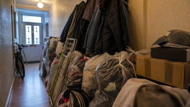 Cluttered hallway in residential apartment with garbage bags, clothes, cardboard boxes and bicycle blocking exit route. Fire safety hazard and evacuation obstruction concept.