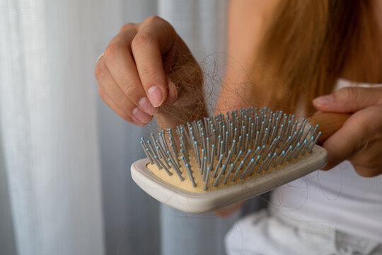 Close-up of woman removing fallen hair from hairbrush, excessive hair loss and shedding concept.