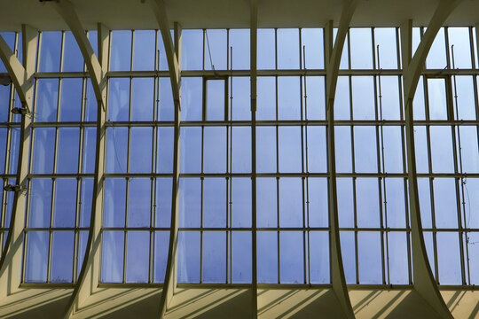 Large-scale glass paneling intersected by angular structural beams against a clear blue sky