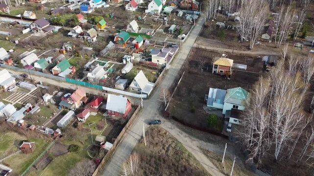 Aerial view of a quiet village with colorful houses. Roads split through green and bare trees. in this tranquil scene. Ideal for rural lifestyle or peaceful community themes