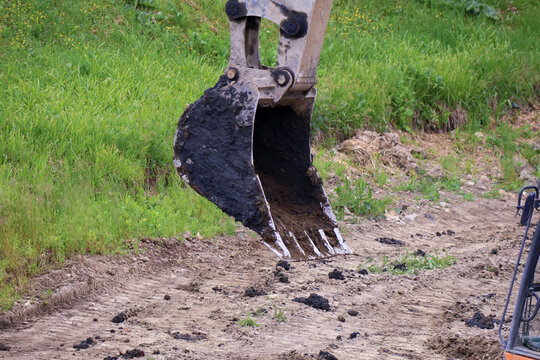 Heavy-duty excavator bucket hovers above loose soil amid green grass and excavated earth