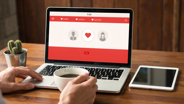 Man's hands typing on laptop with dating app screen and coffee cup on wooden desk