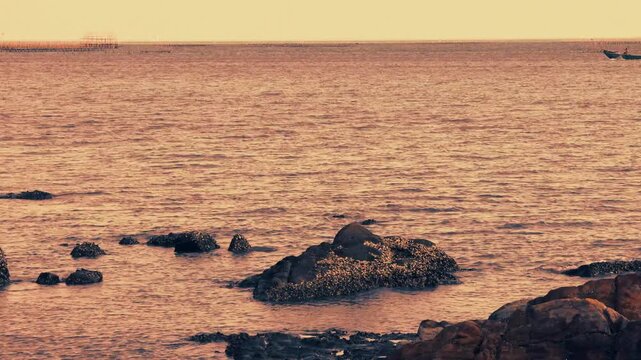 Nostalgic sepia tone seascape featuring rocks in the water and distant coastal aquaculture on the horizon