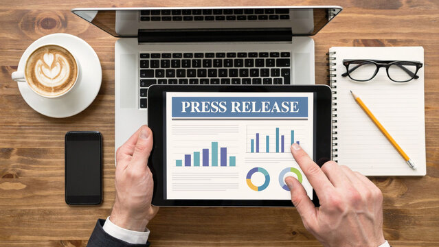 Press release on tablet held by businessman with charts and graphs during morning coffee meeting