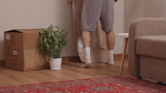 Man entering room and lifting wooden table wrapped in stretch film